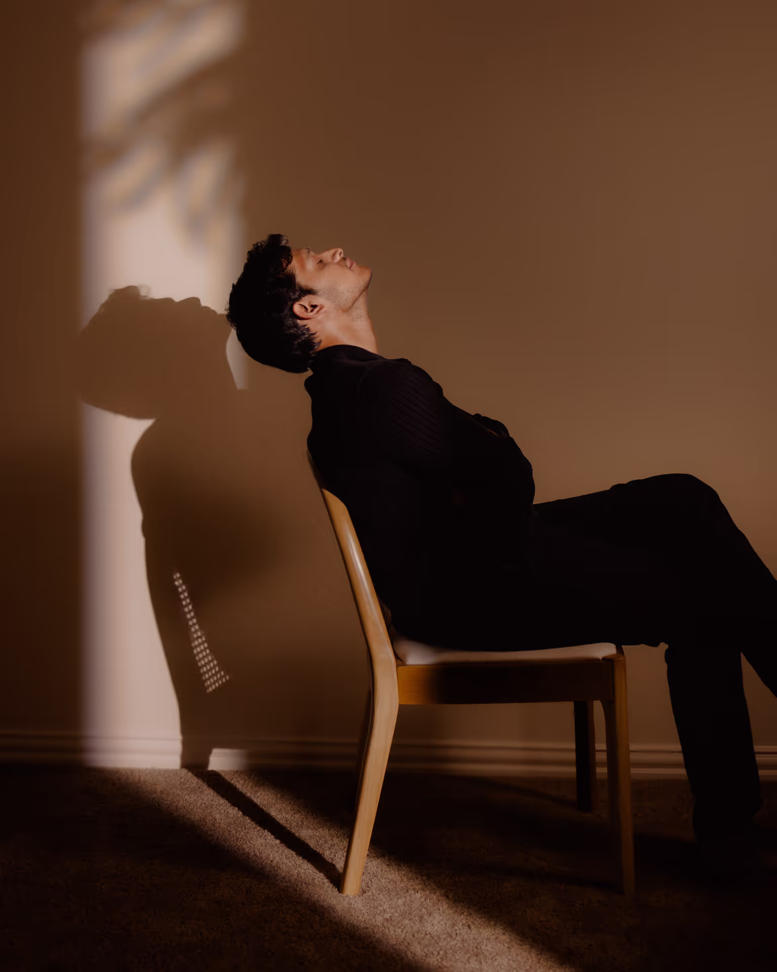 Man sitting in a chair facing up with a shadow on the wall behind.